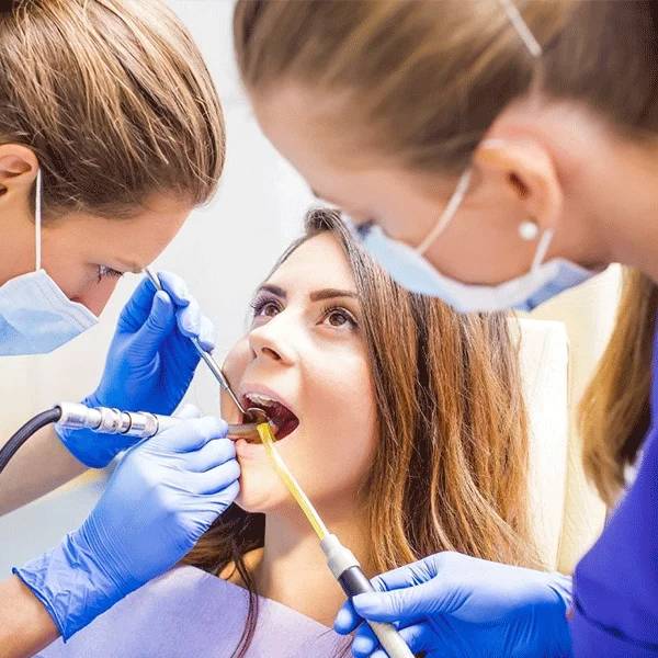 Dental professionals in blue gloves examine a patient's teeth in a bright clinical dental setting
